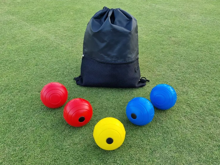 Colorful sports balls with a black drawstring bag on a grassy surface